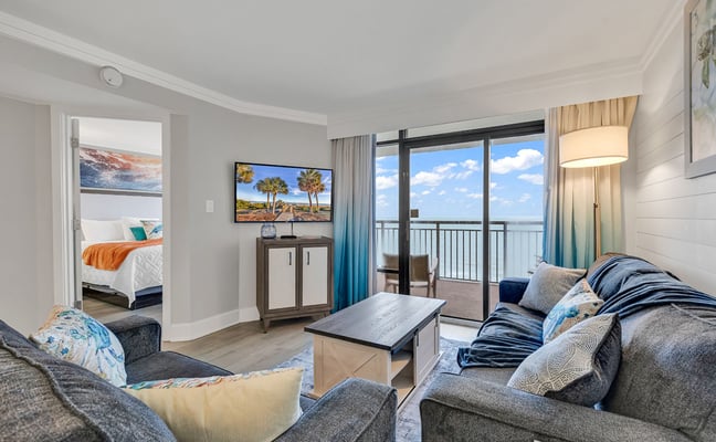 High-rise oceanfront balcony with seating, overlooking beach, RV park, and Atlantic Ocean under blue sky